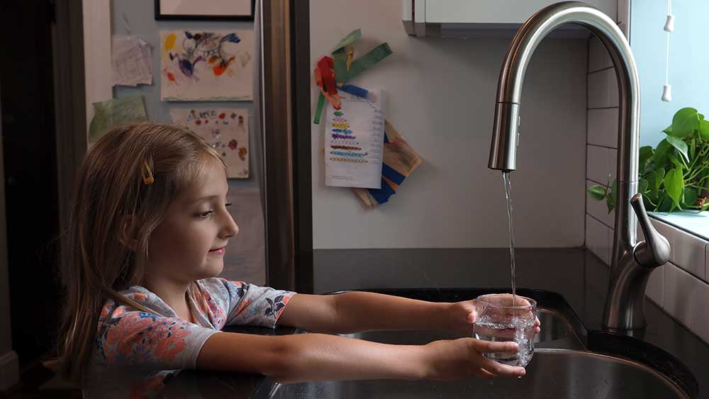 A young girl pours a glass of water from a kitchen tap
