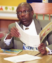 Lionel Brown sits at a table reading a book to students. The long-time education died in May 2014.