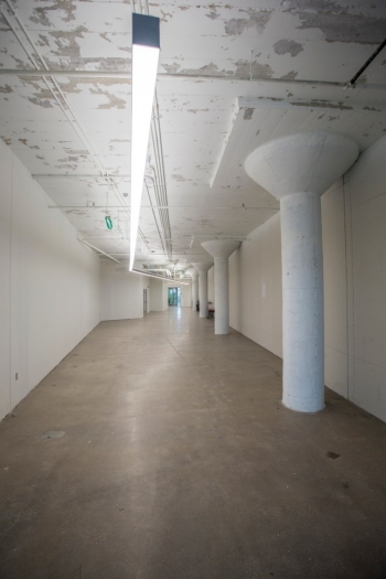 A well-lit hallway with a polished concrete floors and large concrete support pillars. 