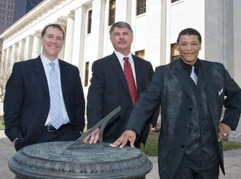 The three men lean against a sundial in front of the statehouse in Columbus.