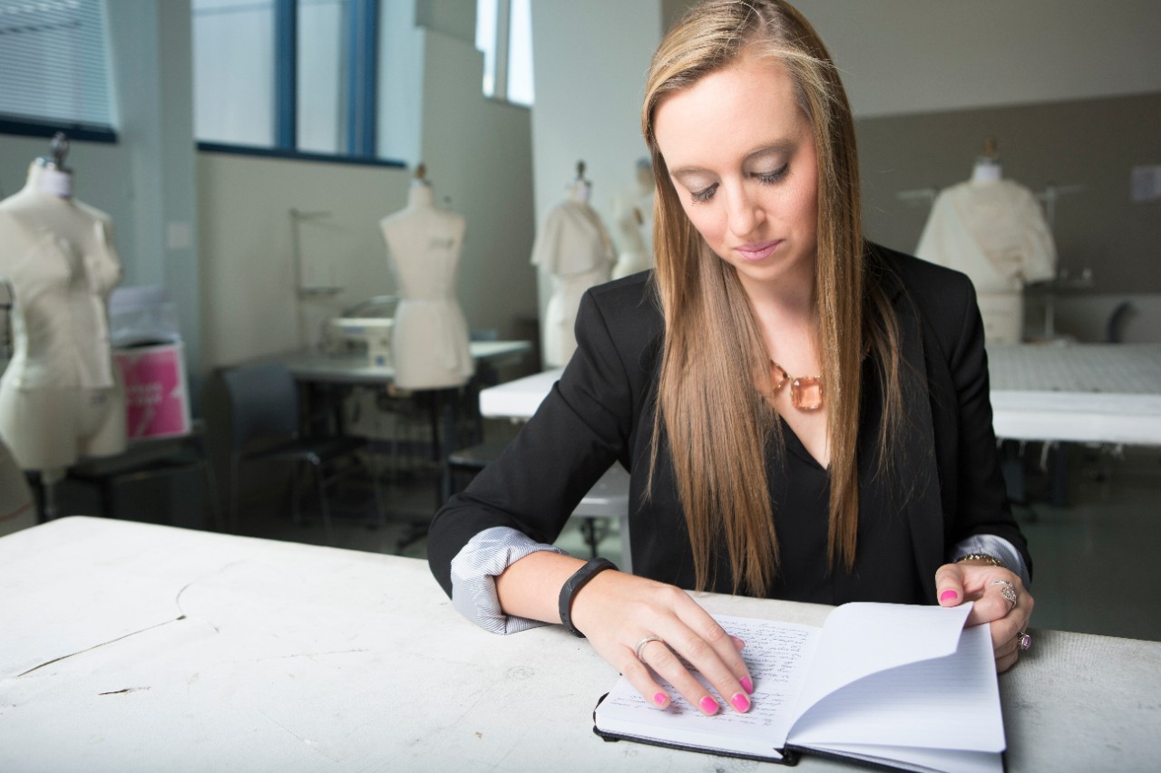 UC DAAP alum sits at a table in a fashion design studio reading a journal