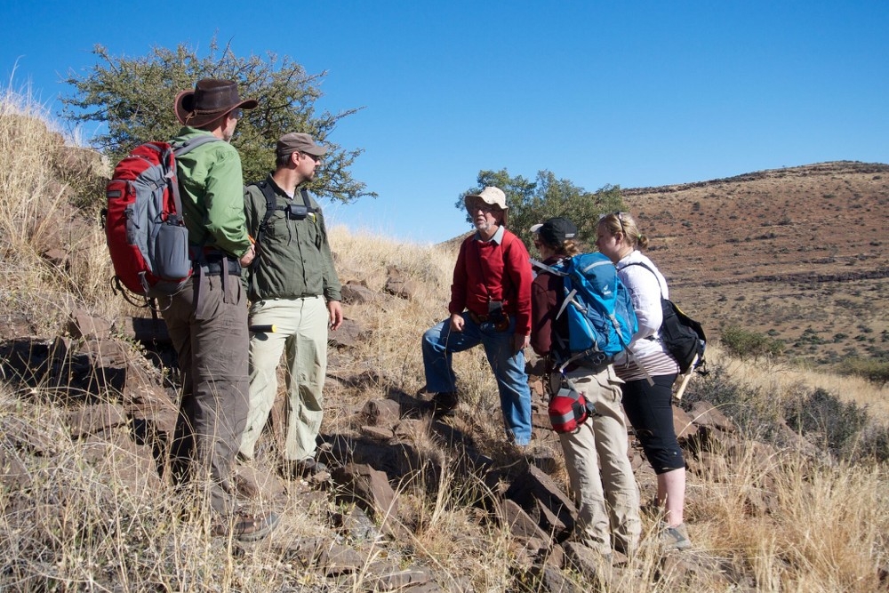 Five scientists stand wearing backpacks on a South African rocky hillside as part of a fossil dig. Photo/Andrew Czaja