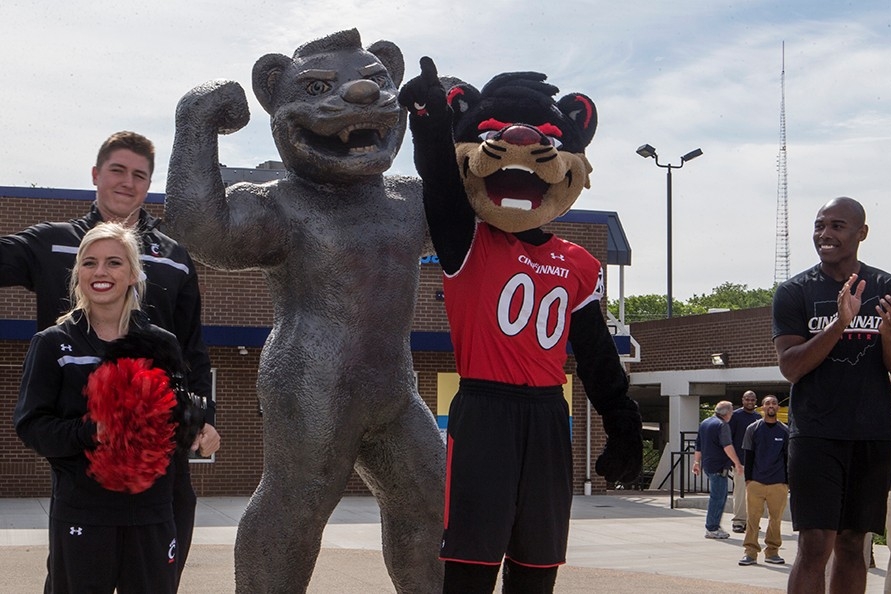 University of Cincinnati cheerleaders and mascot stand next to a new statue of the Bearcat mascot.