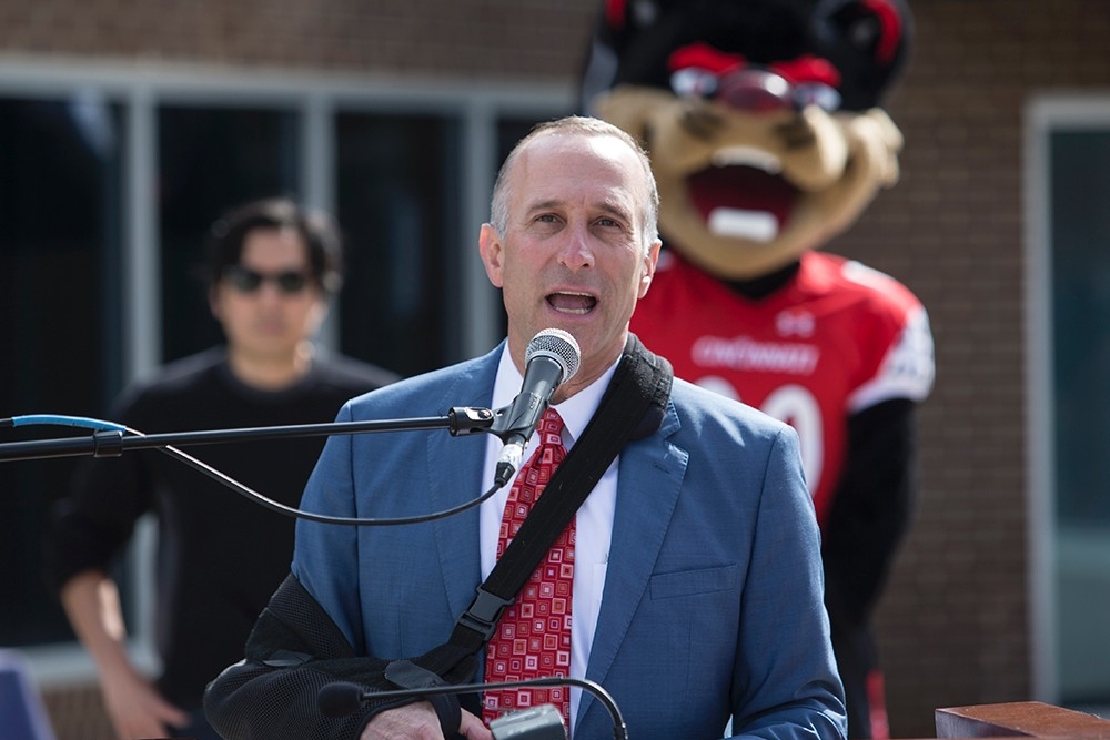 Dan Schimberg, CEO of Uptown Properties, Cincinnati, speaks at a podium during an unveiling of a statue of the University of Cincinnati mascot, the Bearcat.