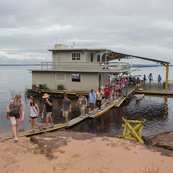  Students walk across a platform from a houseboat onto land.