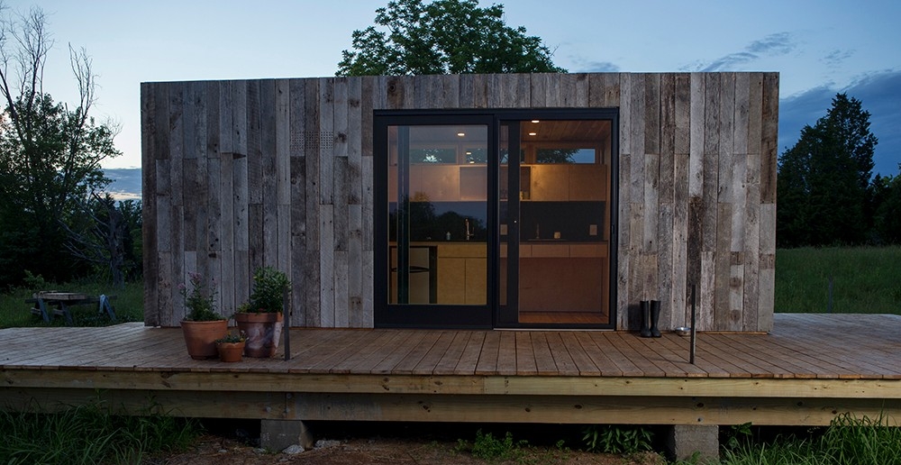 The tiny house has all necessary accoutrements — heating and cooling, a washer, kitchen and bathroom with electric and running water — all within 160 square feet. Photo/Andrew Higley/Creative Services A tiny house sided with reclaimed wood is lit up from within as the sun sets on the Kamama Prairie