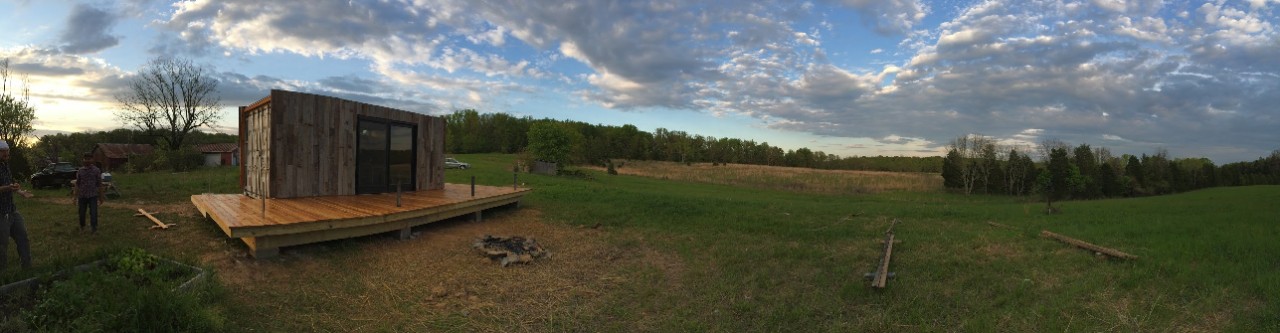 Photo/provided A tiny house with a deck sits on a vast prairie as clouds fill the sky.