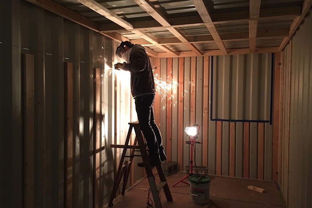 A student welds inside the under-construction tiny house, made from a shipping container.
