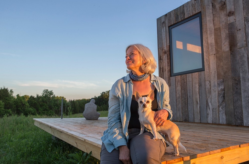 Adrienne Cassel sits with a dog on the deck of her DAAP-constructed tiny house at the Kamama Prairie