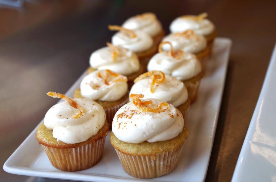 Two rows of cupcakes topped with white icing and candied orange peels, from OCD Cakes.