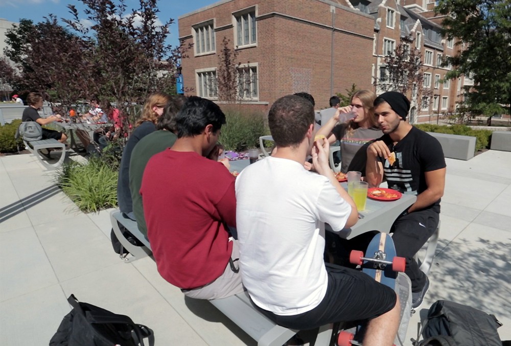 UC students sit at a table and eat food on campus