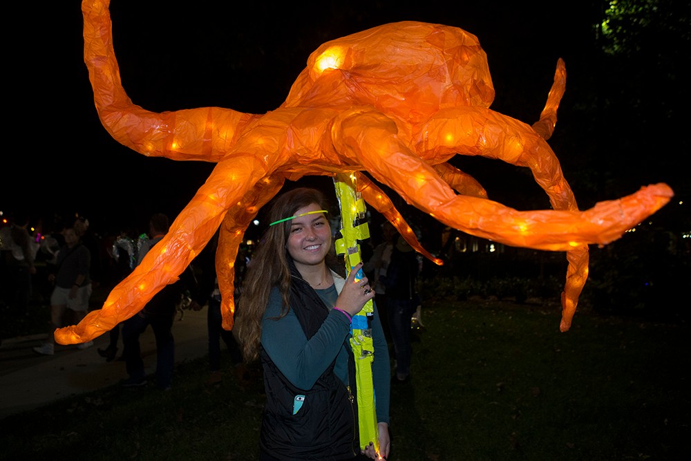 DAAP students display illuminated Body Mantle projects made from inexpensive materials and light-up components. A large orange octopus sculpture is being carried.