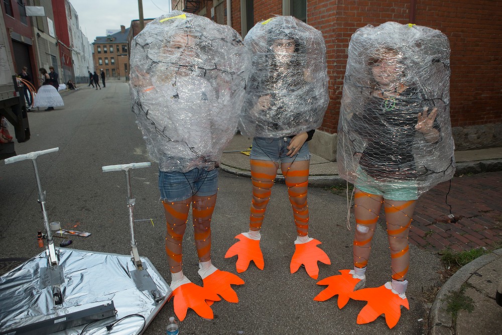 DAAP students display illuminated Body Mantle projects made from inexpensive materials and light-up components. Here, students pose in inflated plastic bags with duck-like orange feet sticking out of the bottom.