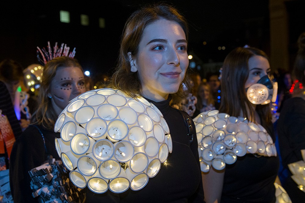 DAAP students display illuminated Body Mantle projects made from inexpensive materials and light-up components. Here, one student wears dozens of plastic disposable cups on her shoulders.