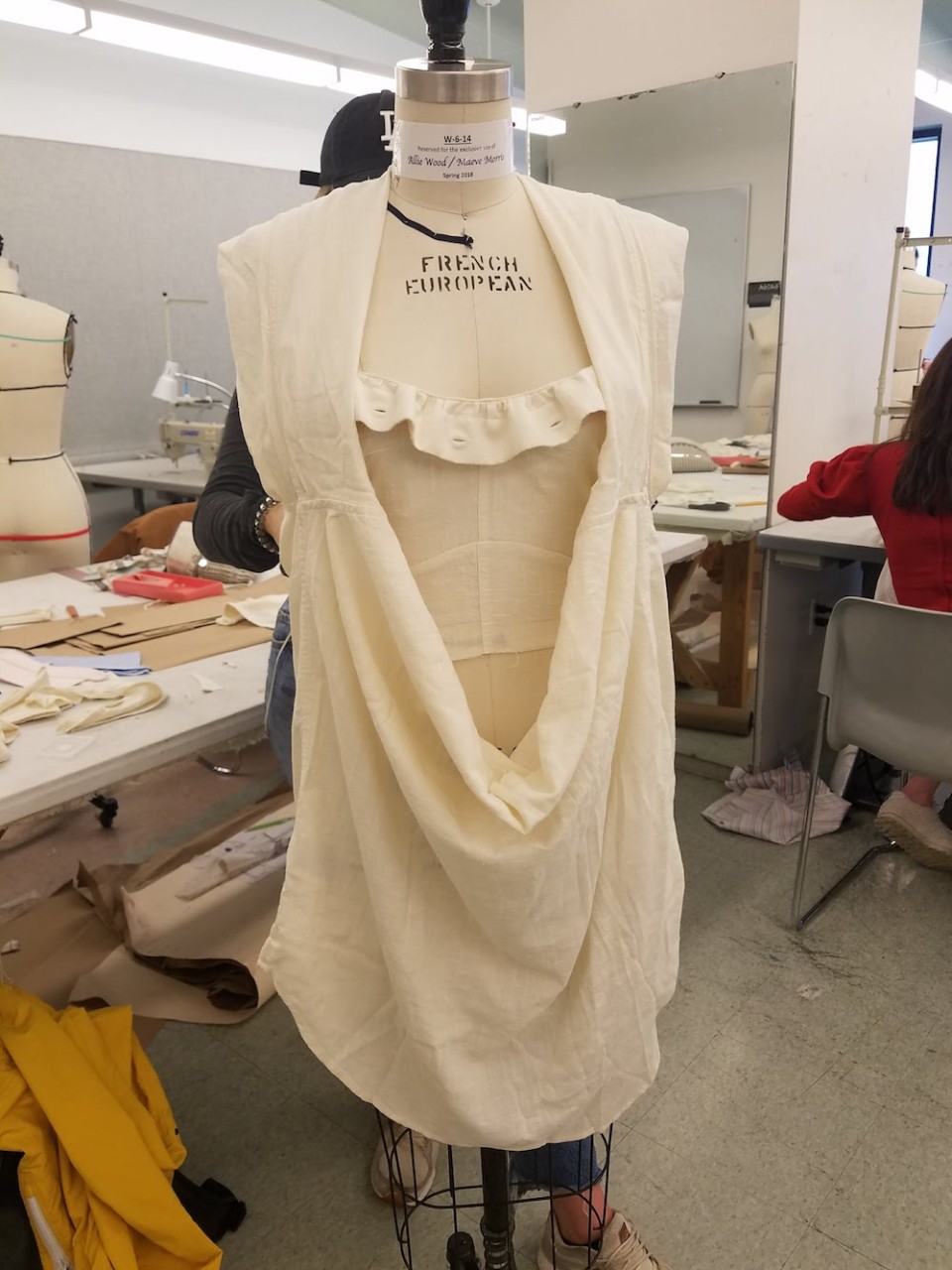 A student fits a garment made from two white button-up shirts on a dress form.