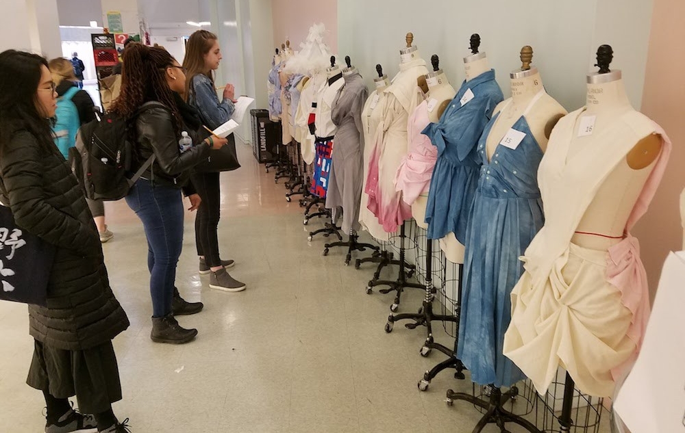 Students look at a line of clothing designs on dress forms