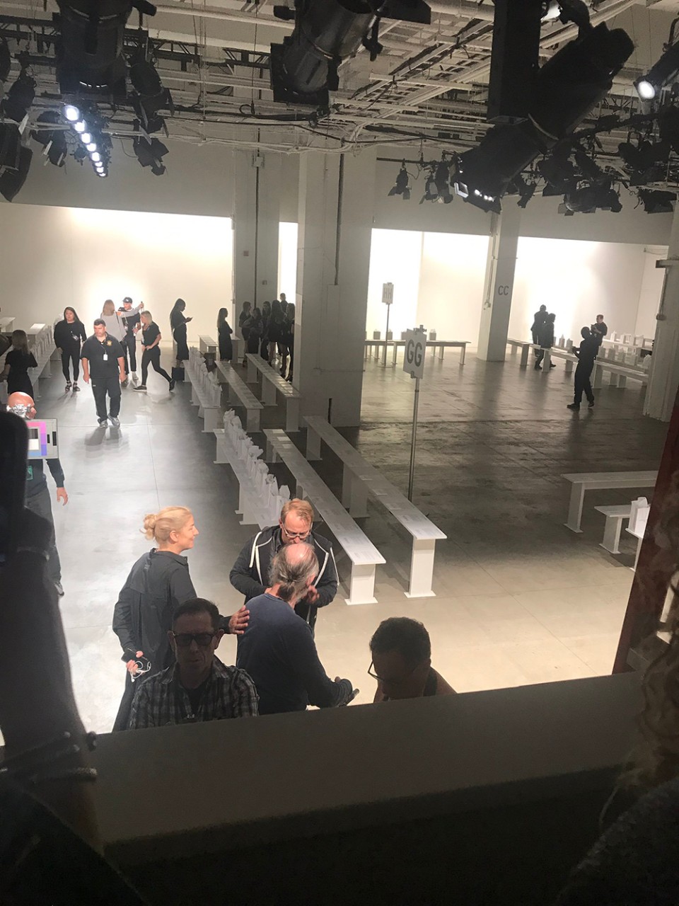 The students toured a gallery where, hours later, a runway show would take place. Pictured is a warehouse-style space with empty white benches with fashion week people walking around the space. 