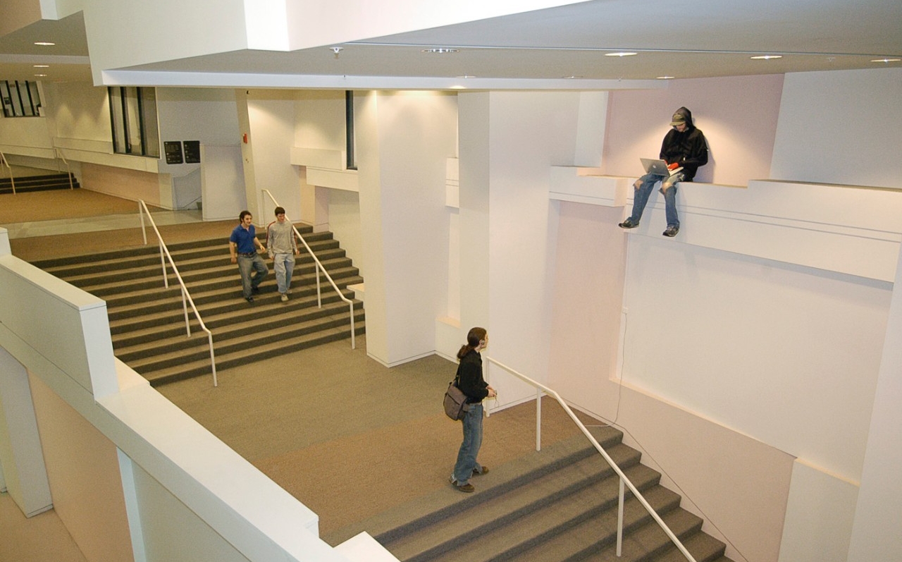 A life-sized sculpture of a student is perched on a ledge high above a stairway.