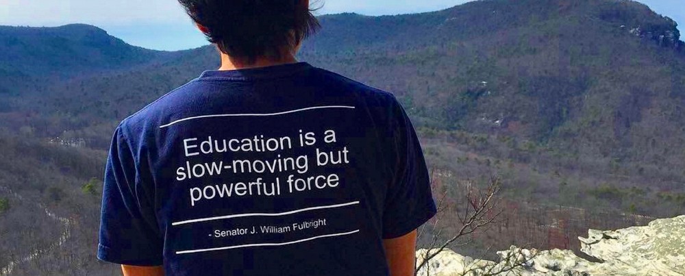 Back of a man wearing a Fulbright Program T-shirt gazing out over a mountain range. photo/courtesy Fulbright Facebook