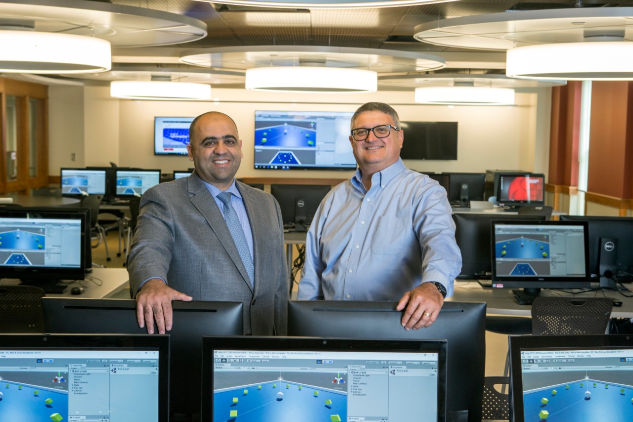 Two men stand in a room filled with computer monitors