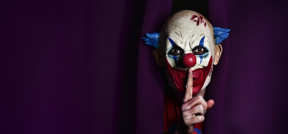 Clown face stares forward holding up a finger to his pursed lips.