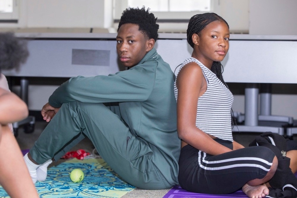 Two CPS students lean against each other during yoga class at UC's Home Base summer camp. photo/Joseph Fuqua II/UC Creative Services
