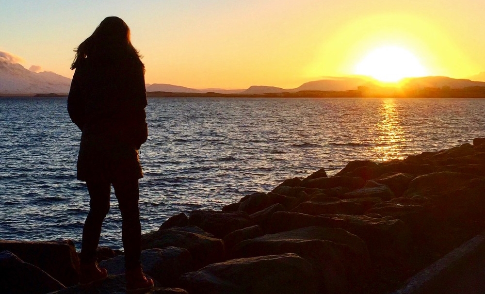 A woman stands on the edge of the water in Iceland looking out over the sunset.photo/Natalie Prager