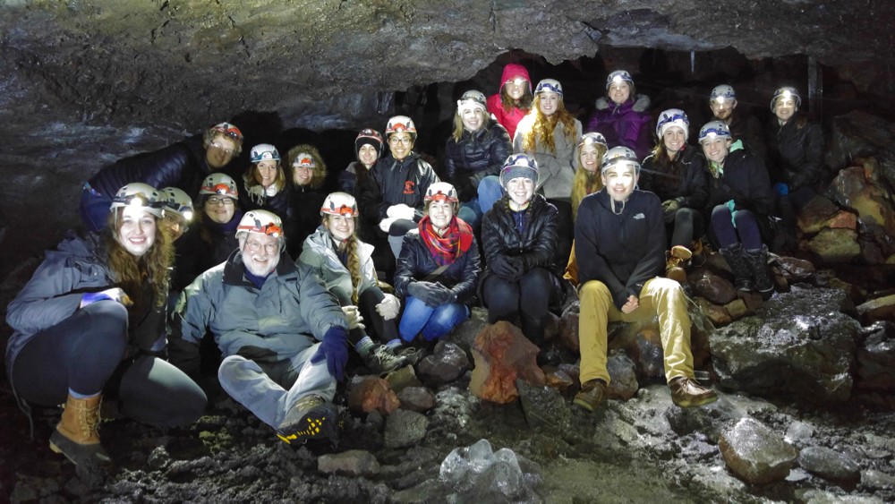 UC study-abroad group sit in a dark lava cave in Iceland wearing hard hats with headlamps.photo/Kevin Grace