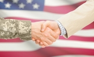 Photo illustration of two in a handshake, one in camoflage, the other a business suit, in front of an American flag