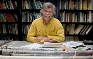 A gray-haired, mustachioed man sits behind a stack of tubes that hold soil samples.