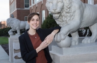 A University of Cincinnati student leaning on one of the university's mascots, a stone lion statue.