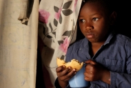 A young black child holds a blue mug and some bread. A photo from the University of Cincinnati-produced documentary on Nairobi.