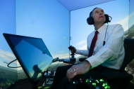 A man appears to flying in the sky with a headphone and microphone. He is surrounded by blue sky in a flight simulator.