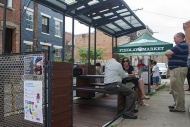A couple relaxes at bench-style tables under a small open roof-- part of a new 'parklet' in downtown Cincinnati.