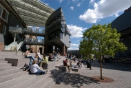 An outdoor area on the campus of the University of Cincinnati, with students sunning themselves on steps outside a modern building.