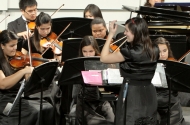 Woman in a black dress in front of an orchestra conducting.