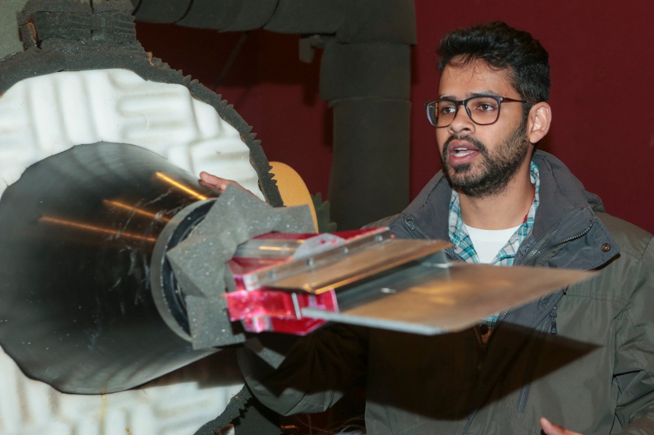 UC doctoral student Aatresh Karnam stands in front of a supersonic jet engine mounted to the floor in an anechoic chamber. UC researchers can affix nozzles of different shapes such as the long, rectangular one pictured. Karnam also attached an adjustable metal plate to the end to study changes in engine noise.