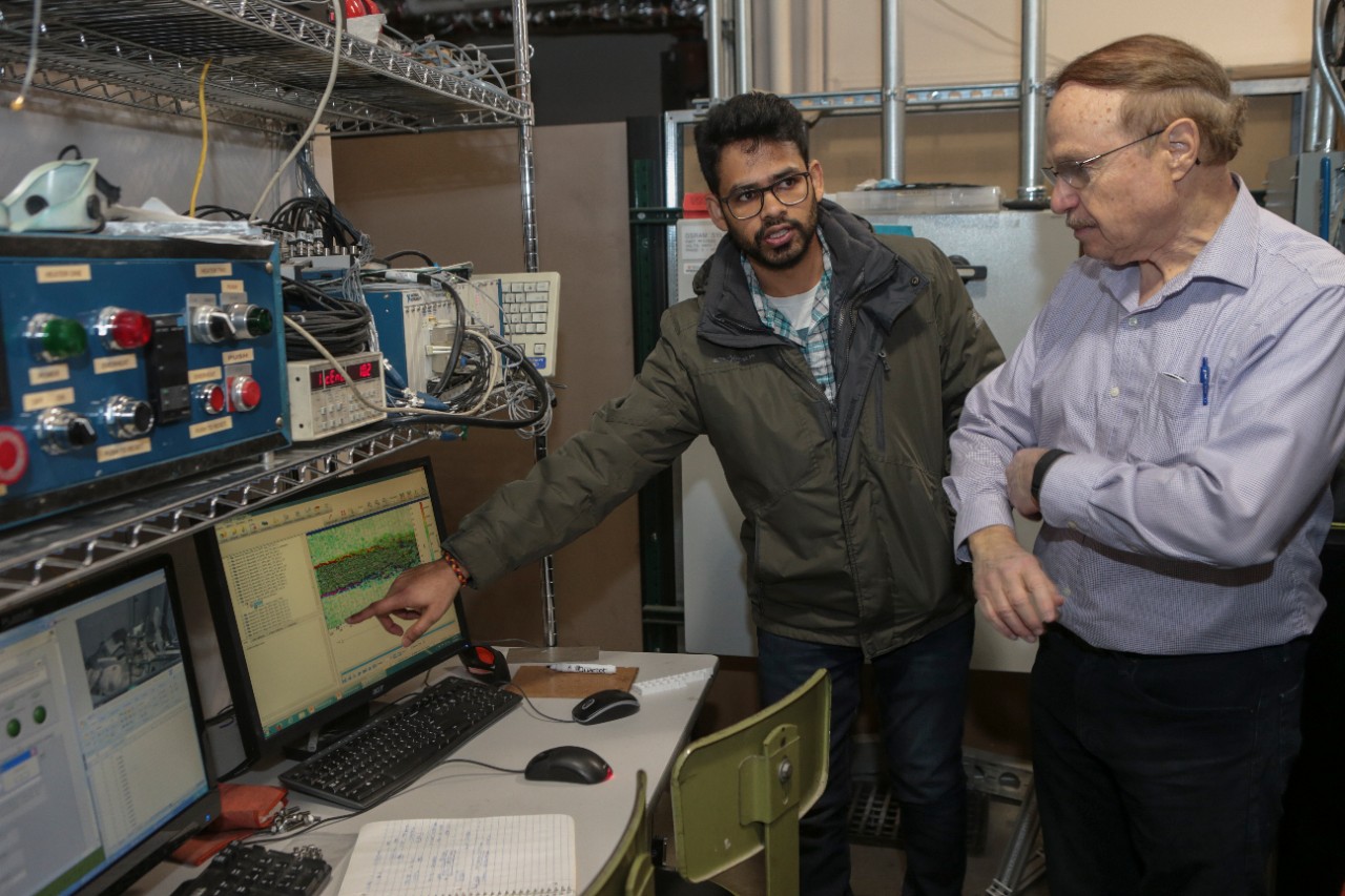 UC doctoral student Aatresh Karnam, left, and UC distinguished professor Ephraim Gutmark discuss the sound map displayed on a computer outside an anechoic chamber where a supersonic jet engine is mounted on the floor. 