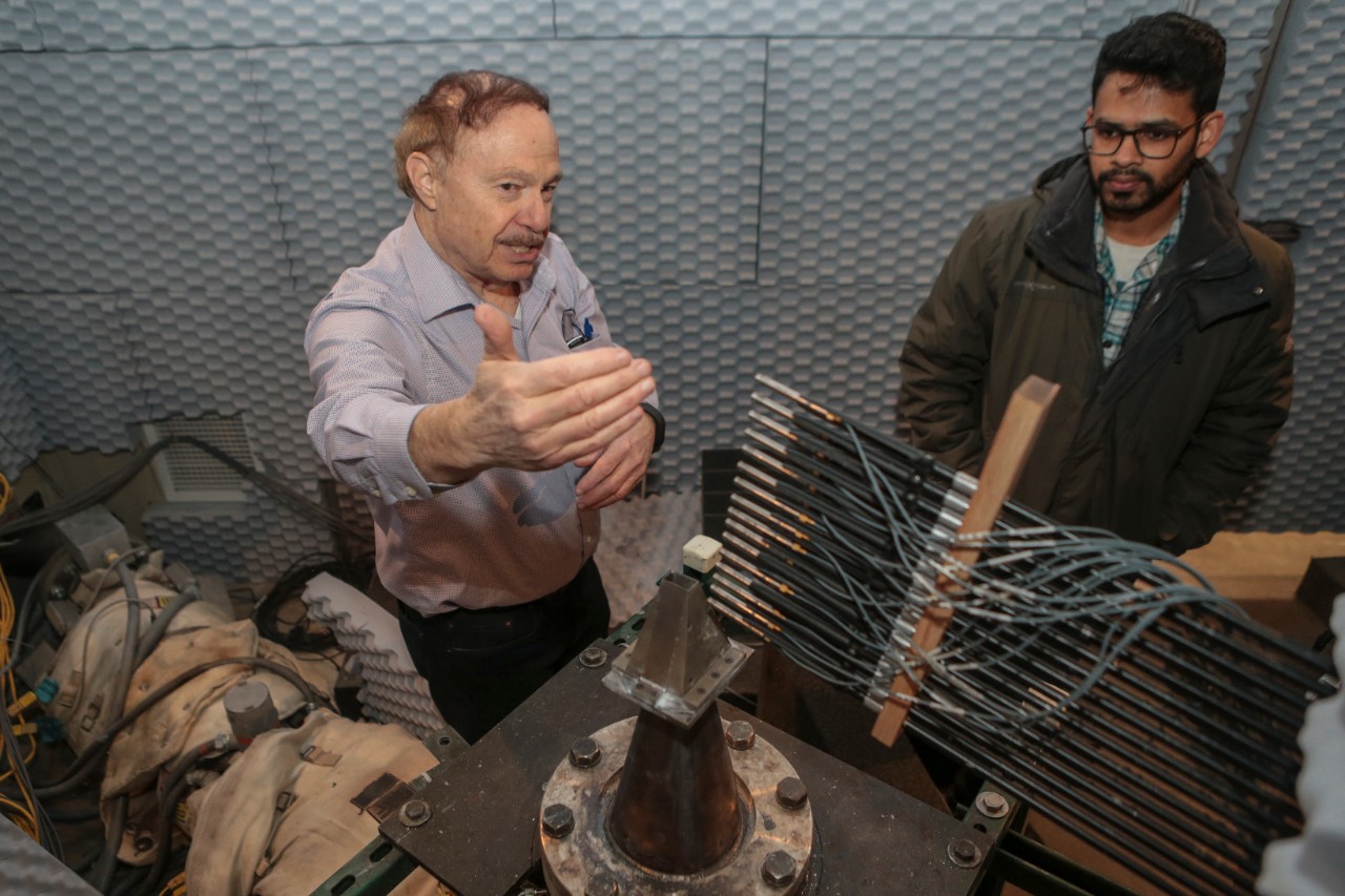 UC distinguished professor Ephraim Gutmark, left, and UC student Aatresh Karnam explain how an array of microphones extending from right to left record sound from a supersonic jet engine mounted to the floor. The anechoic chamber features textured foam panels on every hard surface to dampen sound reflection. 