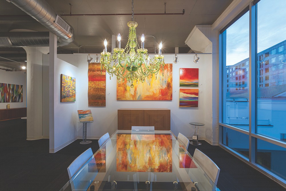 A chandelier, orange-red paintings and glass table fill this area of Art Design Consultants.