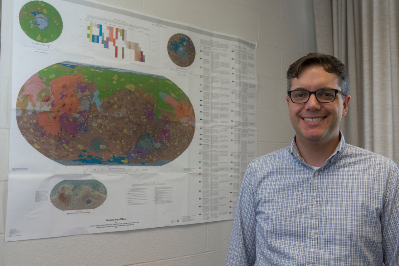 UC geology professor Andrew Czaja in front of a map of Mars in his office.