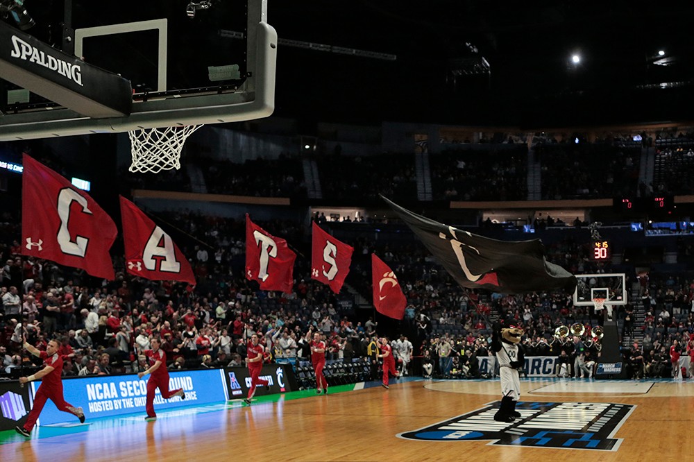 UC cheerleaders run with flags onto the court. 