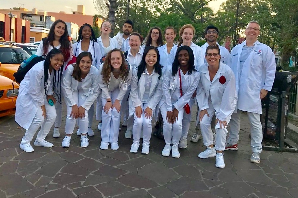 UC undergrads in the first Social Justice Awareness & Global Health Experiences class stand in white medical coats near the Mexican hospital they shadowed during their study abroad trip in 2018.