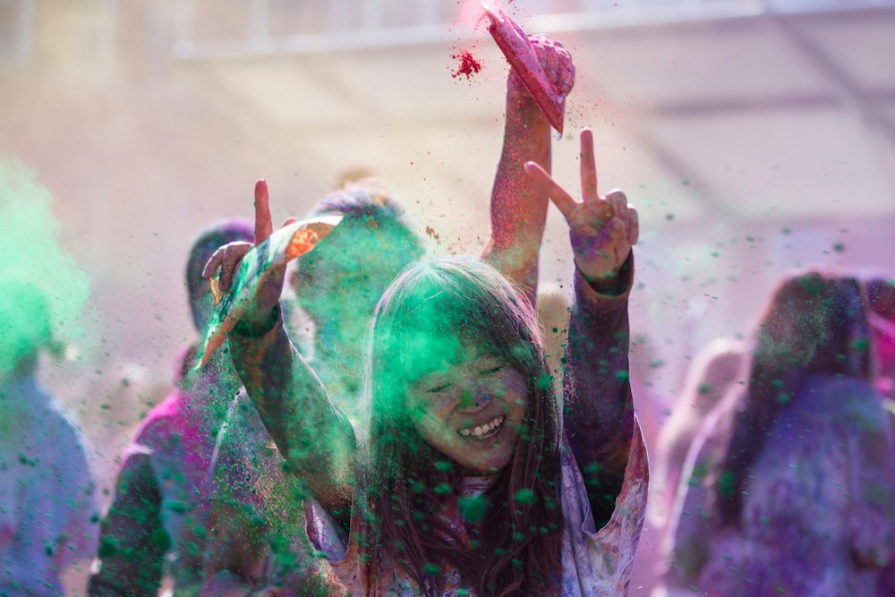 UC student shows peace sign while colored powder flies as part of Holi Festival on campus.