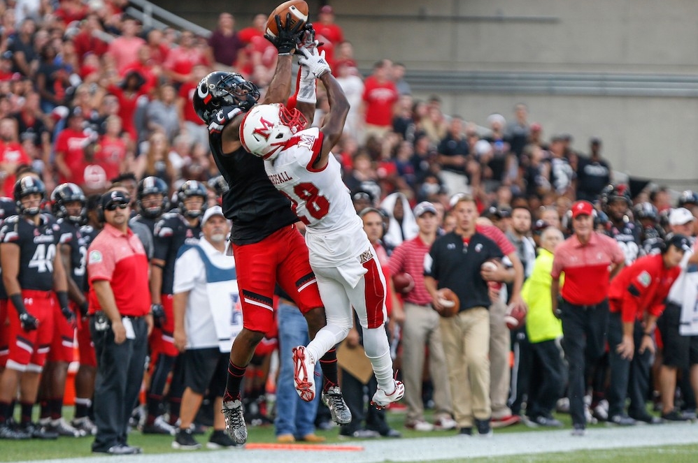UC wide receiver catches football over defender from Miami.
