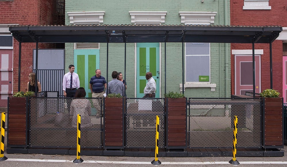 Community members gather inside and around MetroLAB's parklet — a tiny public park located in a street parking spot.