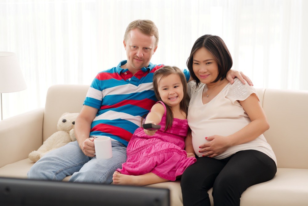 Pregnant woman sits with family on couch watching reality TV. photo/Adobestock