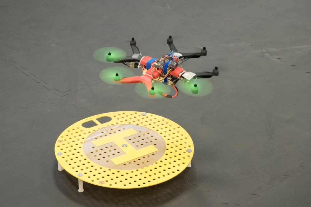 A small octocopter drone hovers over a landing circle.