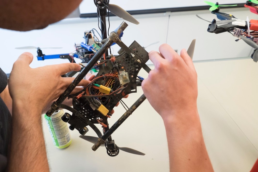 Close-up of UC students' hands as they explain the intricate parts within a four-rotor drone.