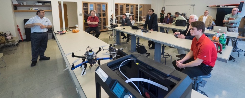 Kelly Cohen, UC professor of aerospace engineering speaks to a group in a room with UVA drones on display